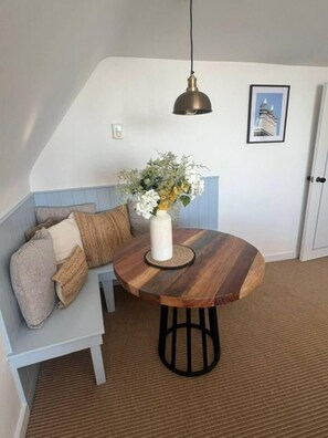 Ein gemütlicher Sitzbereich mit einem runden Holztisch, einem Blumenstrauß und einer Pendelleuchte.