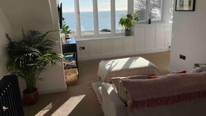 A bedroom with a large window overlooking the sea, a bed, a desk with a plant, and a potted plant beside the bed. - The Turret - The Best View in Folkestone (Folkestone)