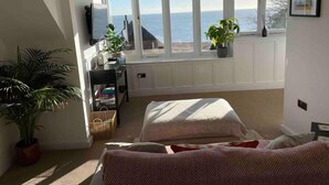A bedroom with a large window overlooking the sea, a bed, a desk with a computer, and several potted plants. - The Turret - The Best View in Folkestone (Folkestone)