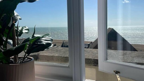 A view from a window overlooking a beach with a potted plant on the windowsill. - The Turret - The Best View in Folkestone (Folkestone)