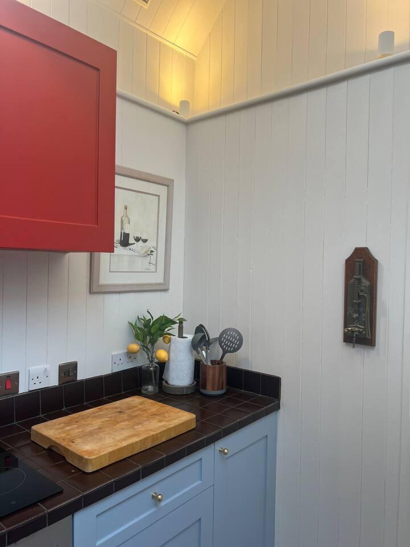 Una cocina con encimera de madera, un armario rojo y un cuadro en la pared.