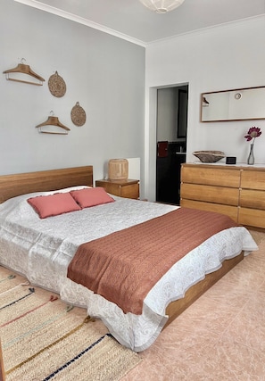 A neatly arranged bedroom with a large bed, a wooden dresser, a mirror, and a hanging light fixture.
