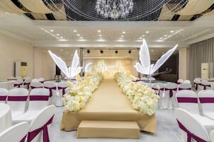Un salón de banquetes con un pasillo central, sillas blancas y una decoración floral.