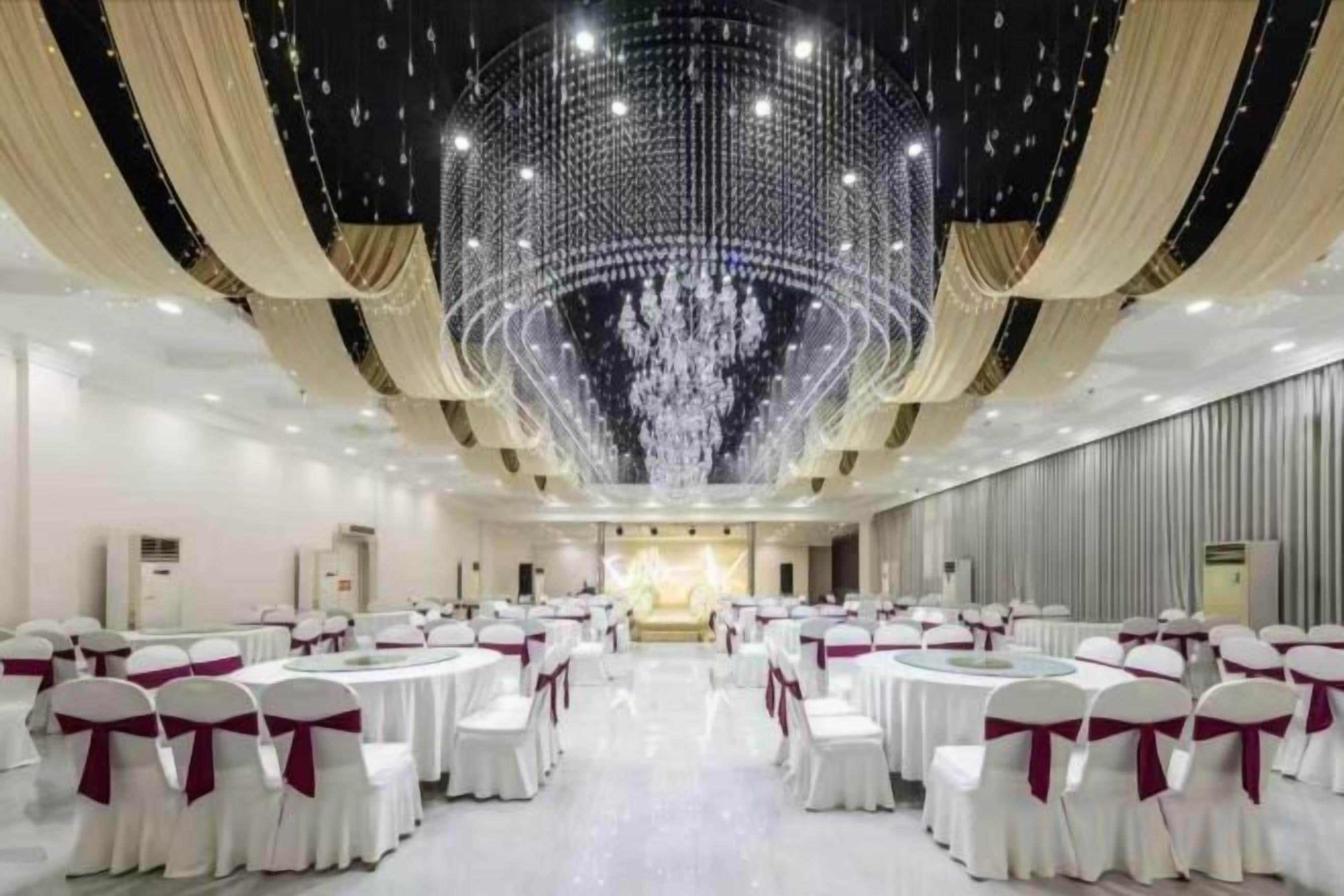 Ein Bankettsaal mit runden Tischen, weißen Stühlen und einer großen Chandelier.