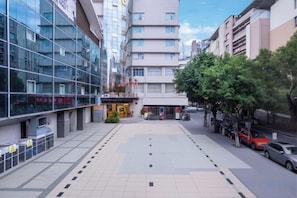 A modern hotel entrance with a glass facade, a covered outdoor seating area, and a parking lot. - Xinhong Hotel (Weiyuan)