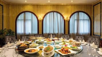 A formal dining room with a round table set for a meal, surrounded by upholstered chairs.