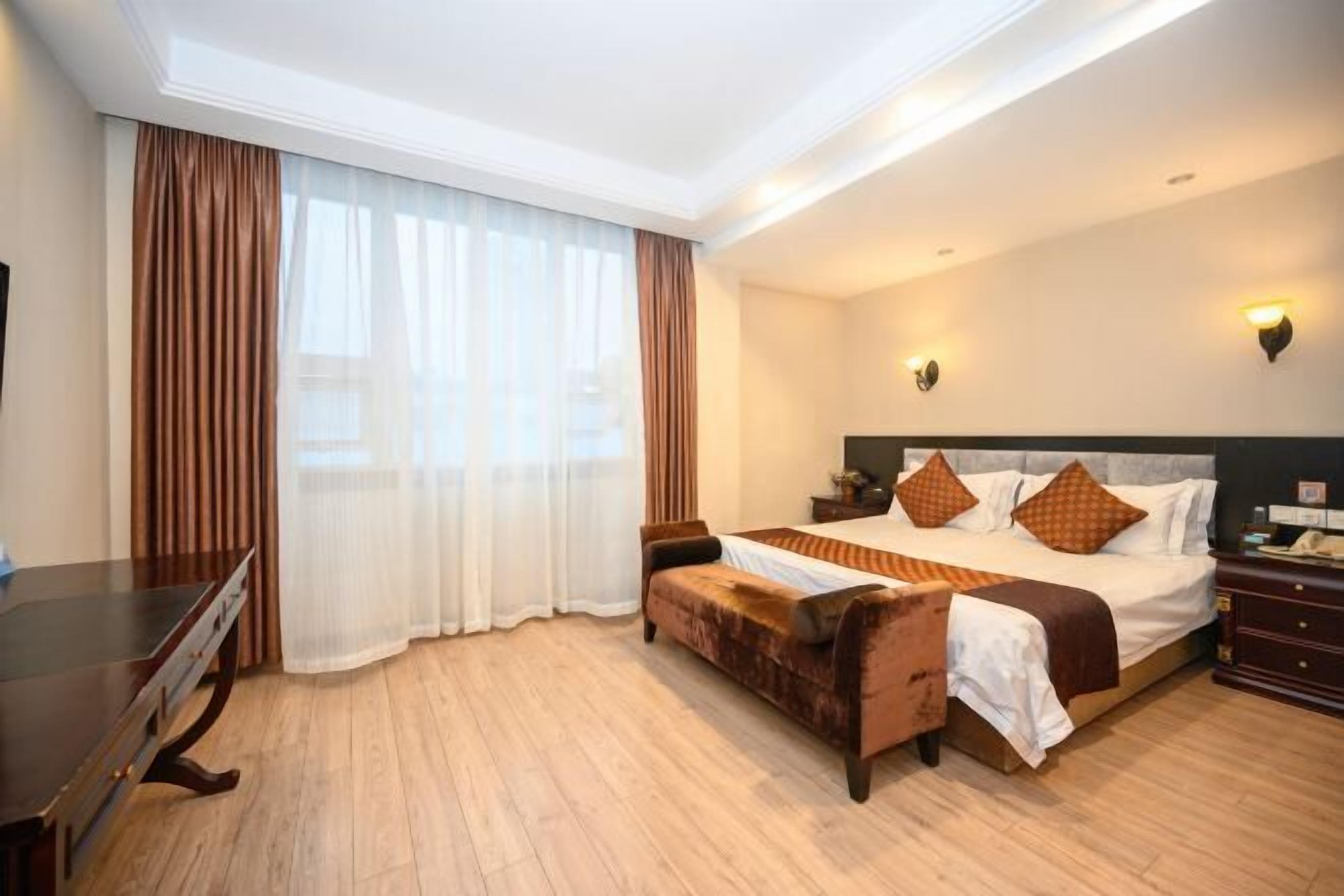 Habitación de hotel con una cama grande, un escritorio de madera, un sofá y una ventana con cortinas.
