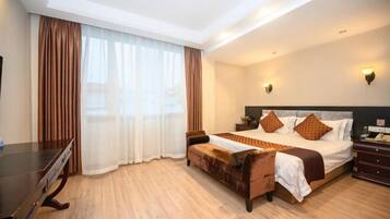 Habitación de hotel con una cama grande, un escritorio de madera, un sofá y una ventana con cortinas.