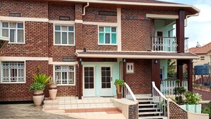 A multi-story brick building with a balcony, large potted plants, and a concrete ground. - Charming 2-bed House in Kigali (Kigali)