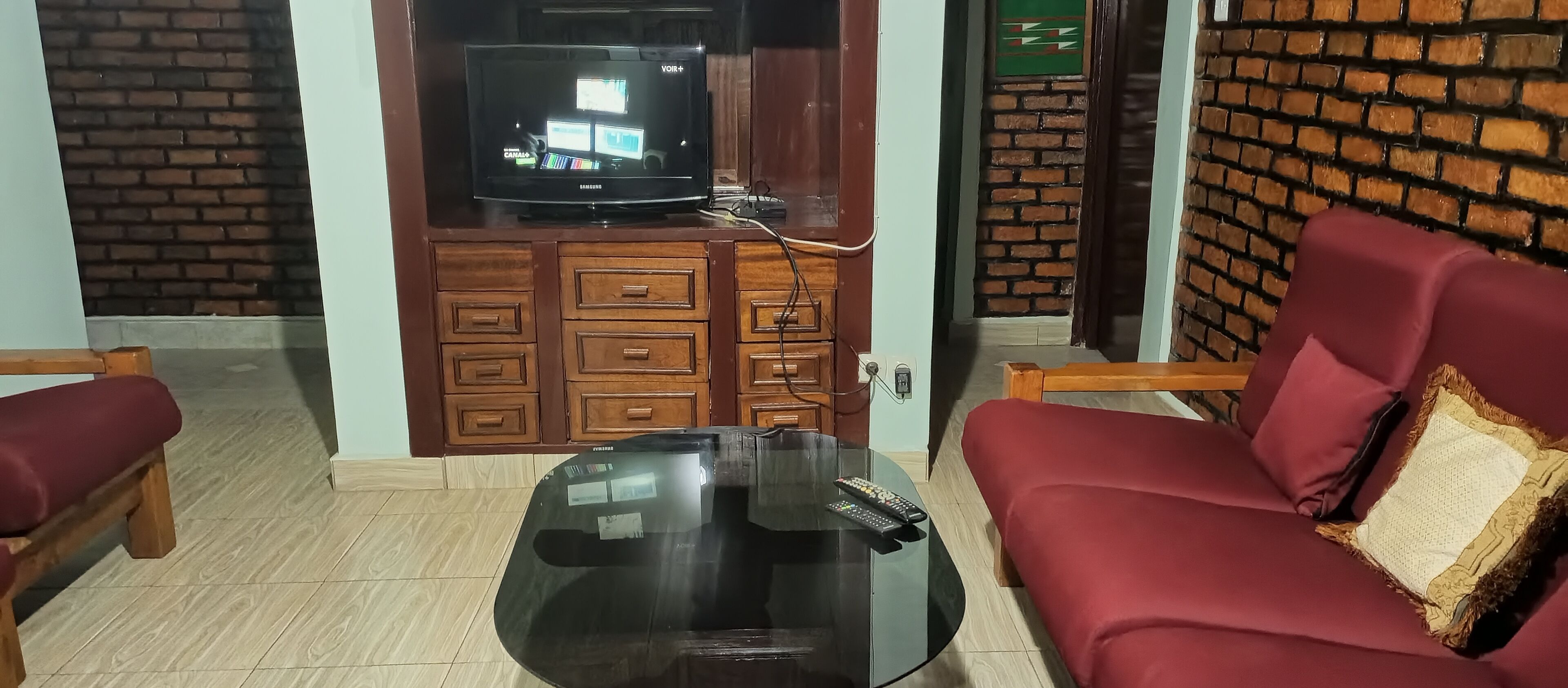 Una sala de estar con televisor, armarios de madera, una mesa de centro de vidrio y un sofá rojo.
