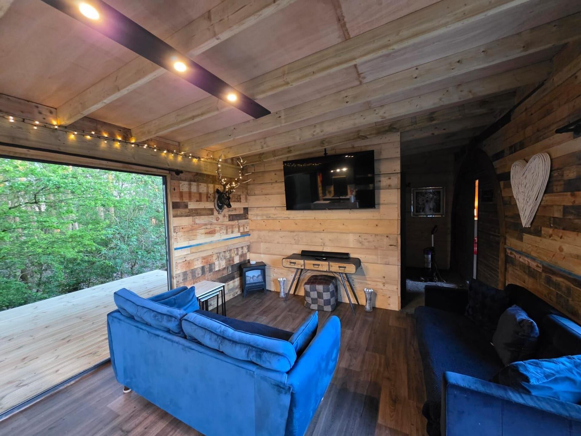 A cozy cabin interior with a blue sofa, a fireplace, and a television mounted on the wall.