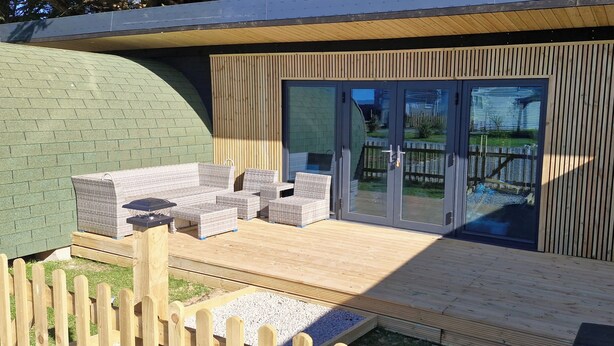 A deck with outdoor furniture, a wooden fence, and a sliding glass door leading to a garden. - Tall Pines Lodge Dog Friendly, Nr Sutton on Sea (Mablethorpe)