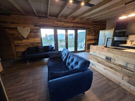 Una sala de estar acogedora con un sofá azul oscuro, una pared de madera con una decoración de corazón y vistas amplias a través de puertas de cristal.