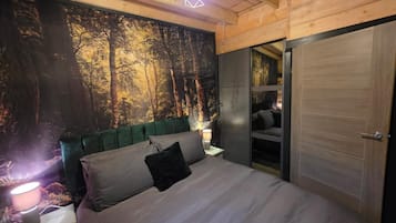 A bedroom with a bed, a nightstand, a lamp, a wall mural, and a door.