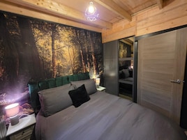 Un dormitorio con cama, mesita de noche, lámpara, un mural en la pared y una puerta.