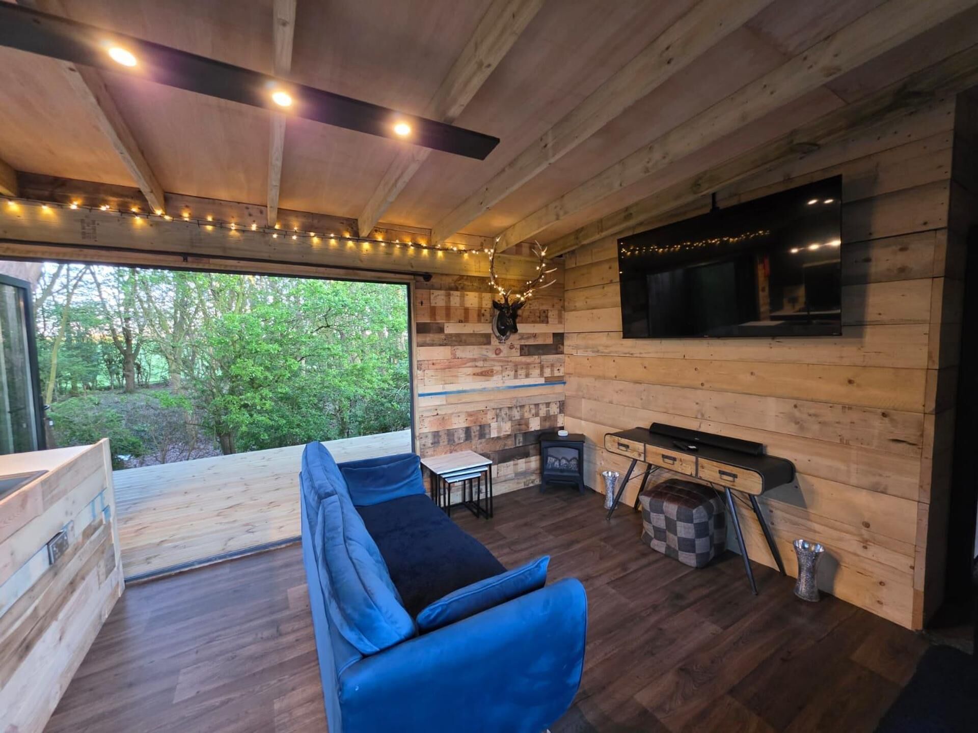 A modern log cabin interior with a sofa, fireplace, TV, and a view of the forest.