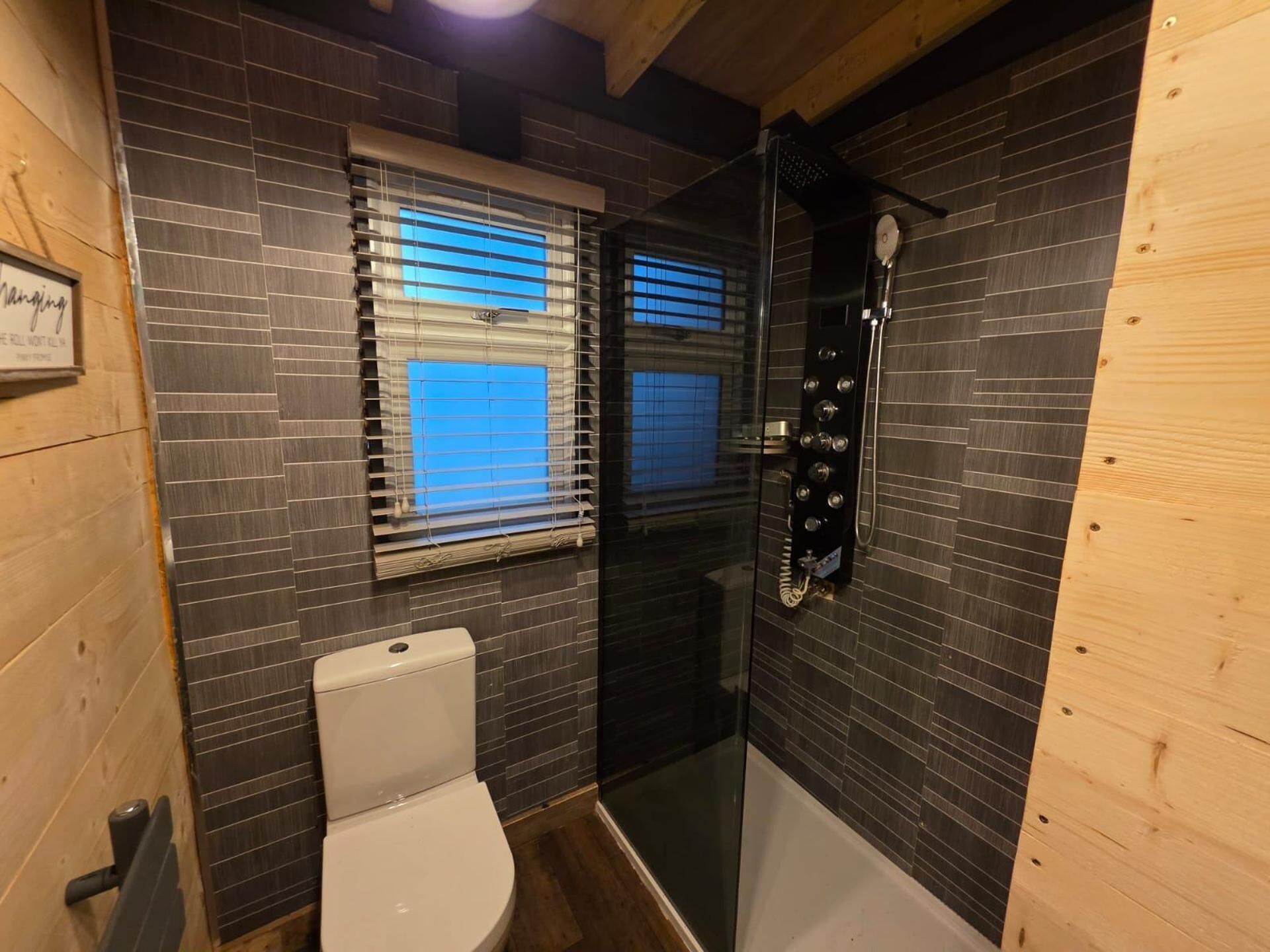Ein kleines Badezimmer mit Toilette, Dusche und einem Fenster mit Jalousien.