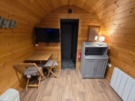 Interior acogedor de una cabaña de madera con televisor, una pequeña mesa con sillas, un armario y un radiador.