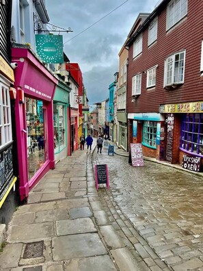 A narrow cobblestone street lined with colorful buildings, including shops and a visible 'The Epic Shop' sign.