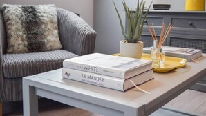 Un salon moderne avec un canapé gris, une table basse blanche et deux livres intitulés « WHITE » et « LE MANOIR ».