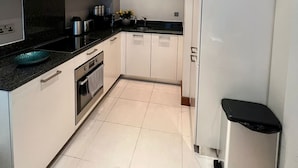 Una cocina moderna con armarios blancos, encimera negra, electrodomésticos de acero inoxidable y un elemento decorativo en la pared.