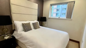 Un dormitorio ordenado con una cama grande, dos mesitas de noche y una ventana que ofrece vistas al exterior.