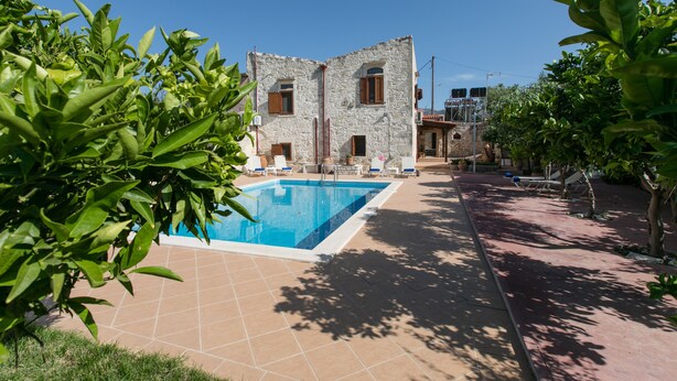 A pool area with a stone building in the background, surrounded by greenery. - Pool Villa Afroditi for 10 Persons in Margarites (Mylopotamos)