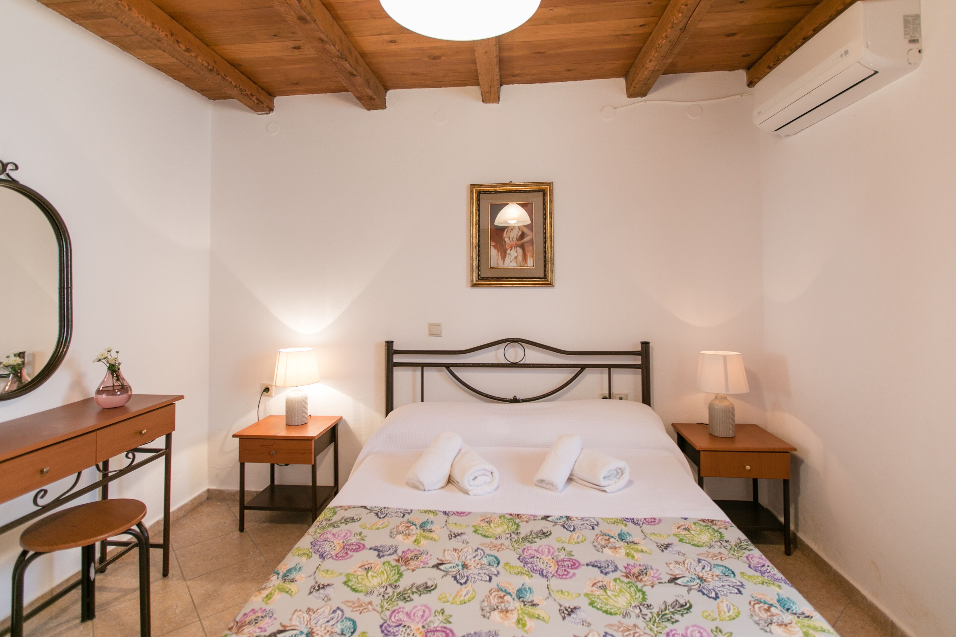 A bedroom with a bed, two bedside tables, a nightstand, a dresser, a mirror, and a framed picture on the wall.