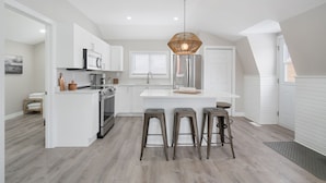 A modern kitchen with white cabinetry, stainless steel appliances, and a central island with stools. - Beautiful newly renovated home w/ canal view (Port Colborne)