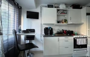 Een kleine keuken met witte kasten, een fornuis en een spoelbak.