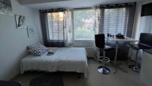 A small, compact room with a single bed, a desk, and a chair. There are curtains on the windows, and artwork on the walls. - Casa South Studio in the Center of Stockholms Soho (Stockholm)