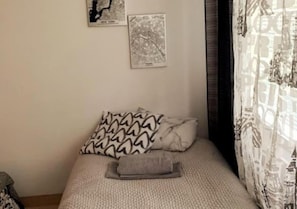 Een slaapkamer met een bed, gestreepte kussens en twee wereldkaarten.