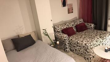 A bedroom with a bed, a sofa, a small table with candles, and a wall-mounted shelf with decorative items.