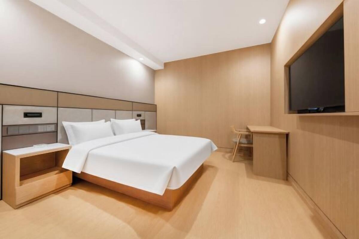 Een moderne hotelkamer met een bed, nachtkastje, televisie en een klein bureau.
