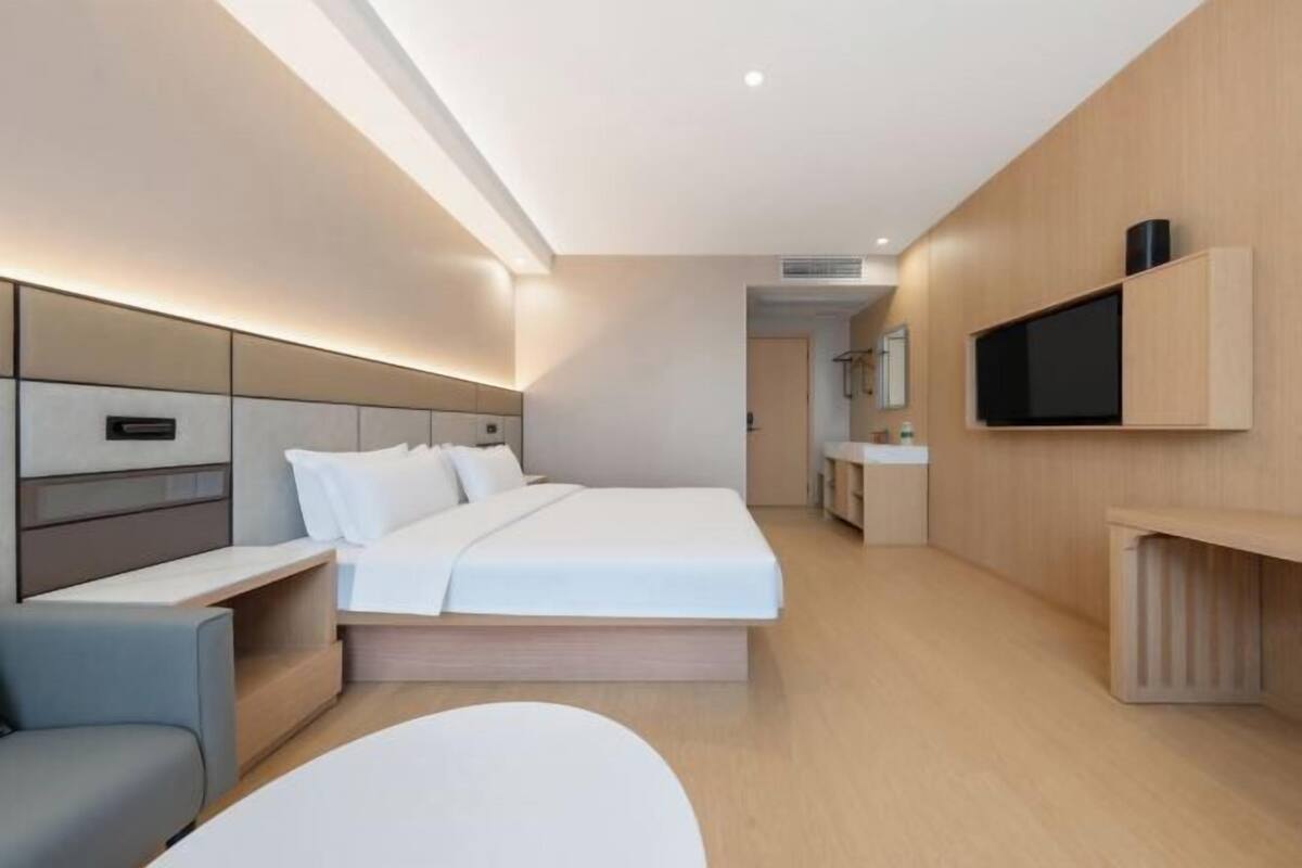 Een moderne hotelkamer met een bed, nachtkastje, televisie en een zithoekje.