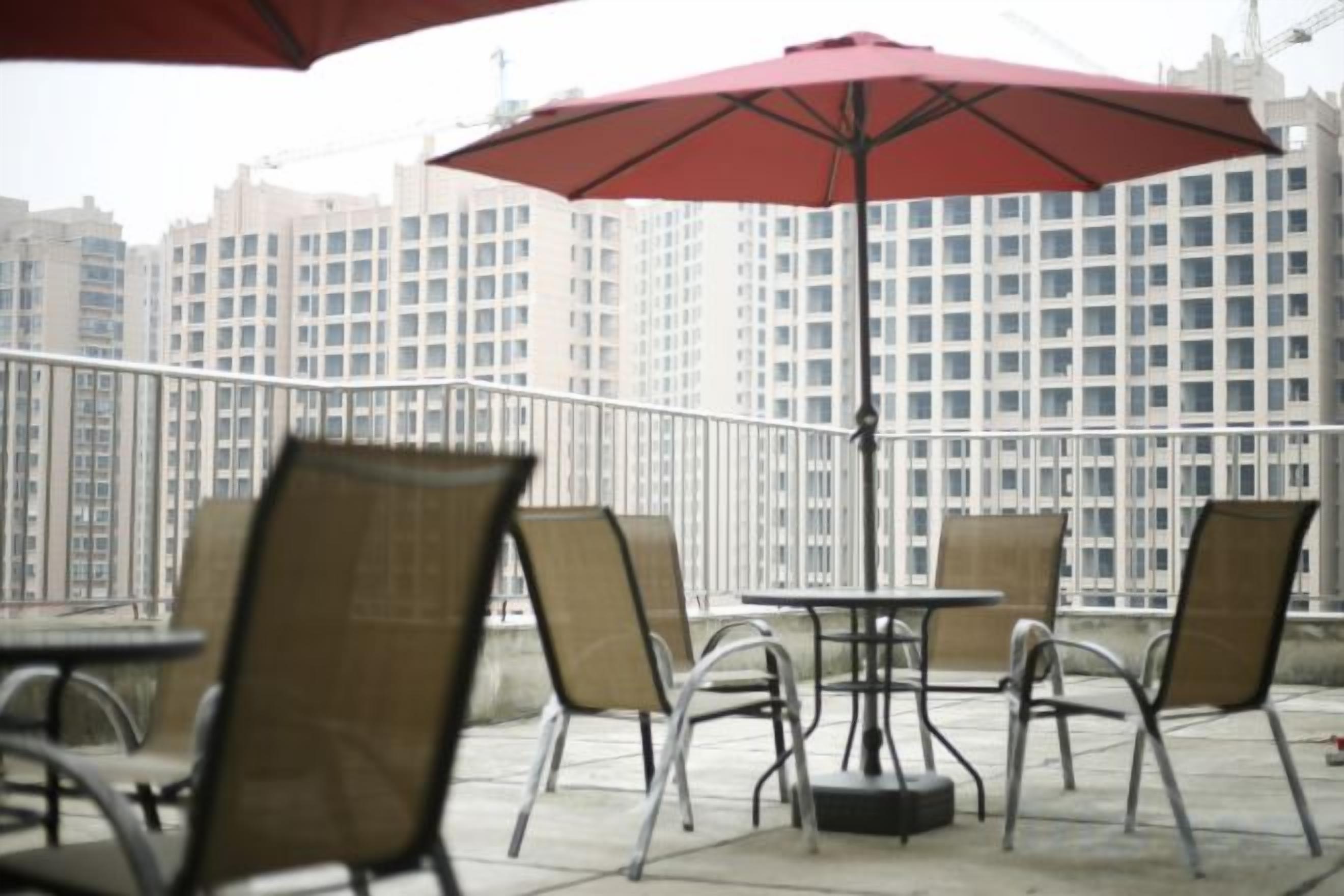 Mobiliario de exterior en la terraza con mesas y sillas, un paraguas rojo y una vista panorámica de la ciudad al fondo.