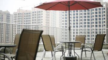 Mobiliario de exterior en la terraza con mesas y sillas, un paraguas rojo y una vista panorámica de la ciudad al fondo.