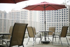 Mobiliario de exterior en la terraza con mesas y sillas, un paraguas rojo y una vista panorámica de la ciudad al fondo.