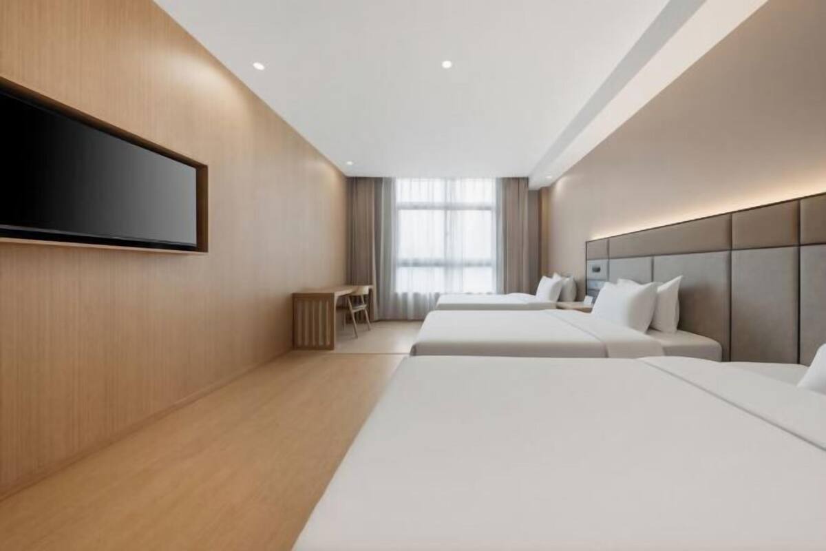 Een moderne hotelkamer met twee bedden, een flatscreen televisie aan de muur, een bureau en een raam met gordijnen.