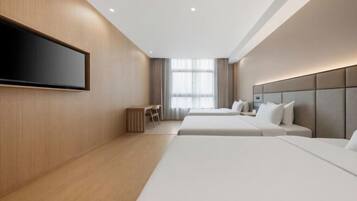 Una habitación de hotel moderna con dos camas, un televisor de pantalla plana montado en la pared, un escritorio y una ventana con cortinas.