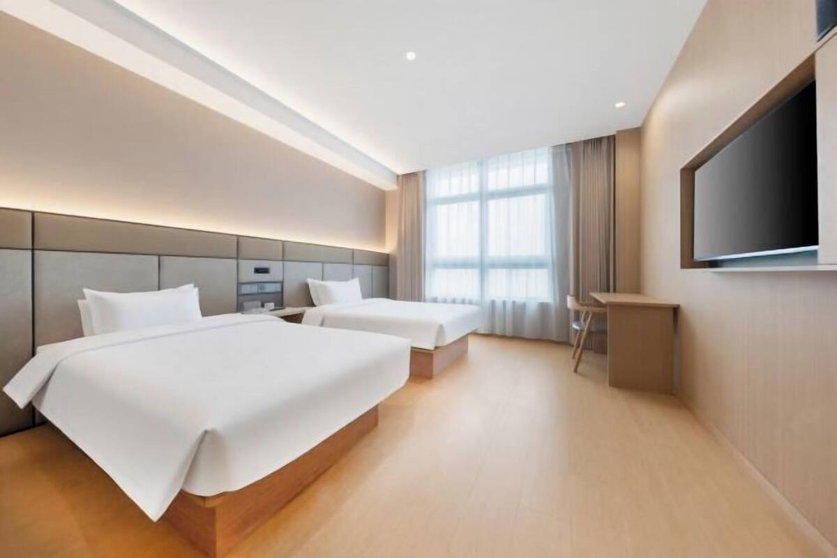 Een moderne hotelkamer met twee bedden, een televisie, een bureau en een groot raam.