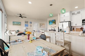 A modern kitchen with white cabinets, a refrigerator, and a dining area with a wooden table and chairs.