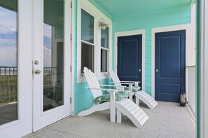A turquoise house with white doors and windows, two white Adirondack chairs, and a small dog statue.