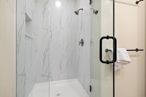 A glass-enclosed shower with a white marble wall, a towel rack, and a showerhead.