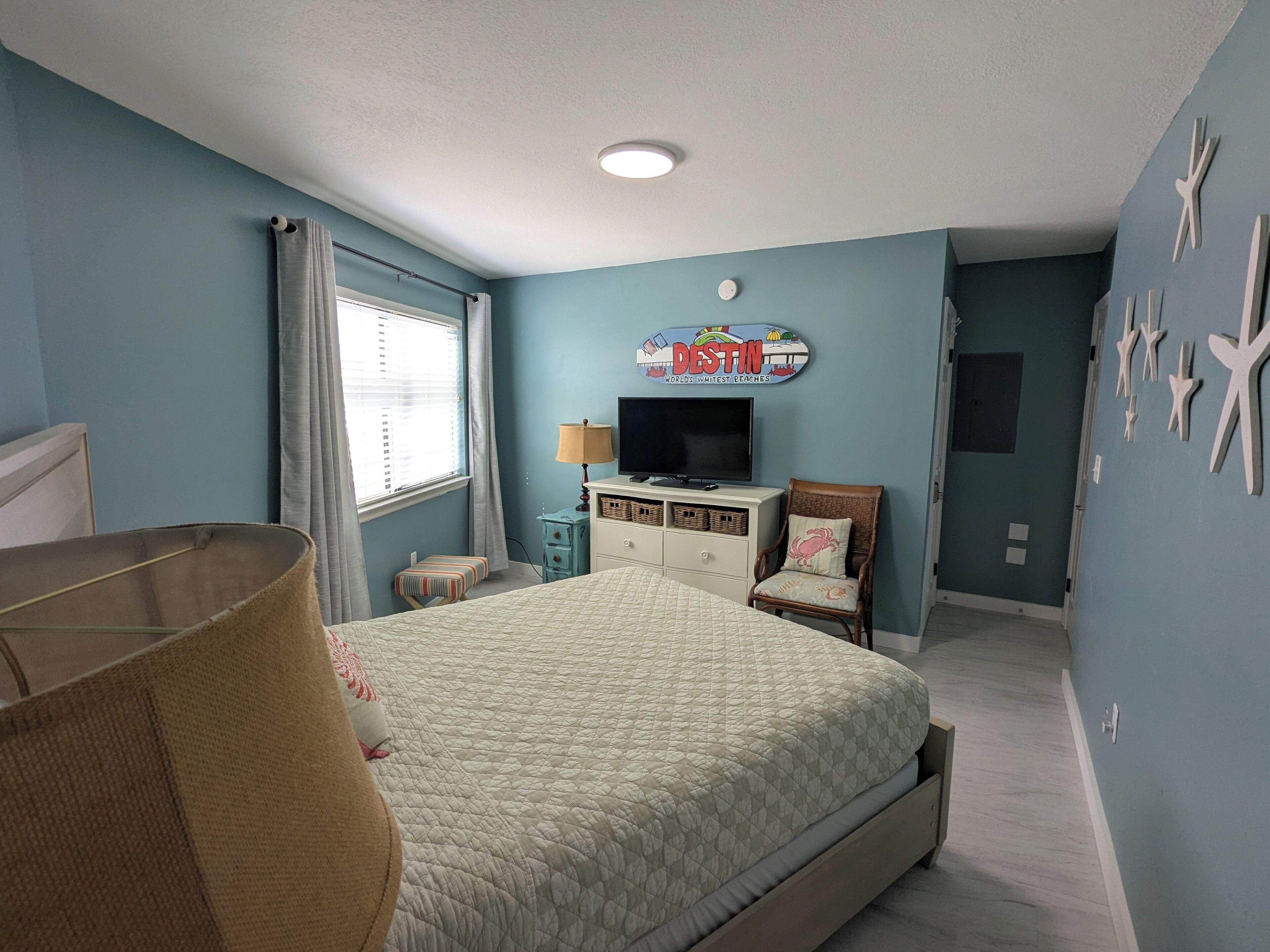 A bedroom with a bed, a television, a small table, a chair, and a wall decoration.