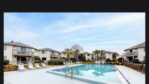 Une piscine entourée de chaises longues, elle-même bordée d’immeubles d’habitation.