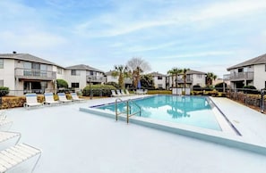 Une piscine entourée de chaises longues, elle-même bordée d’immeubles d’habitation.