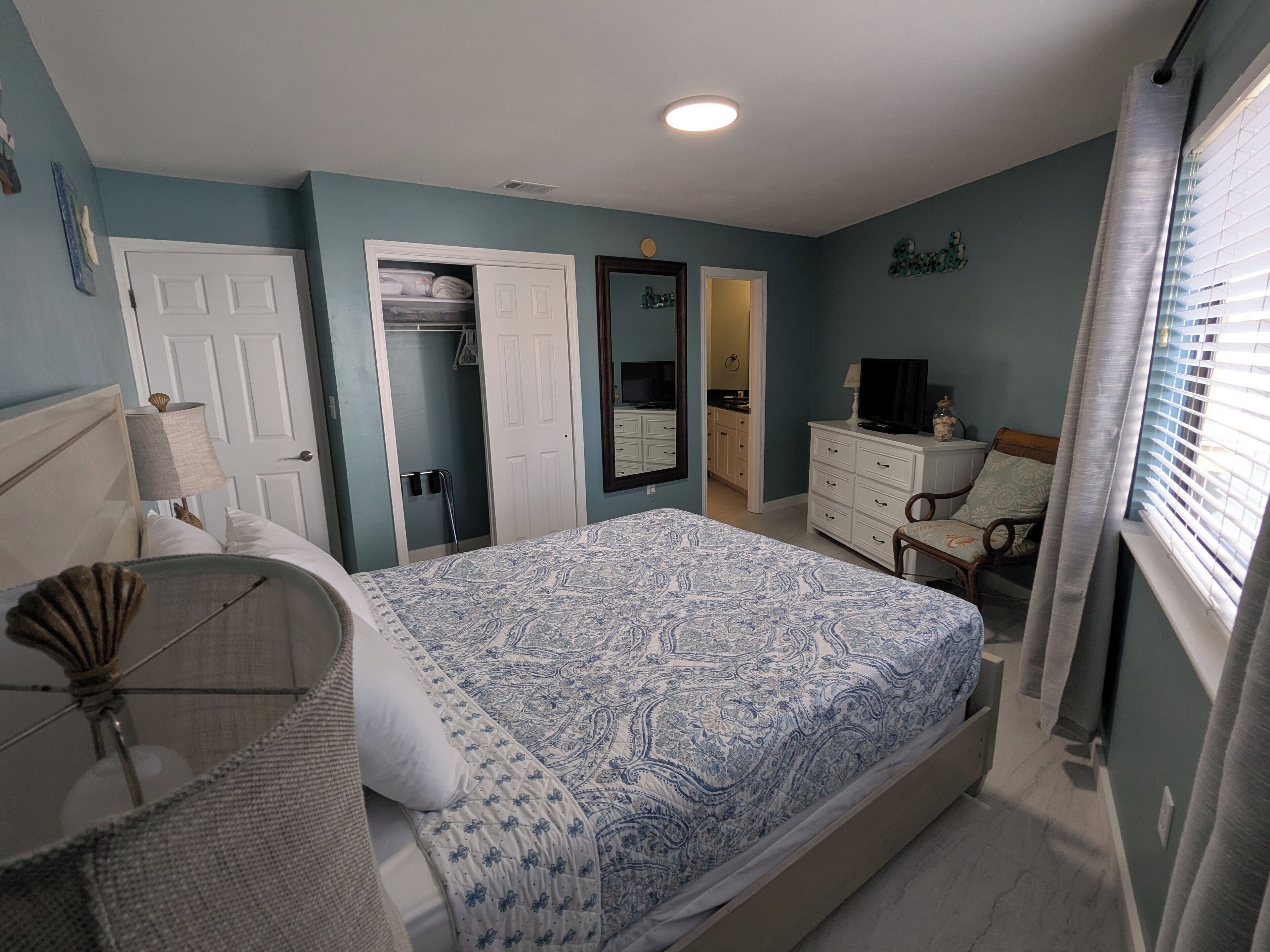 A bedroom with a bed, a dresser, a chair, a mirror, and a closet.