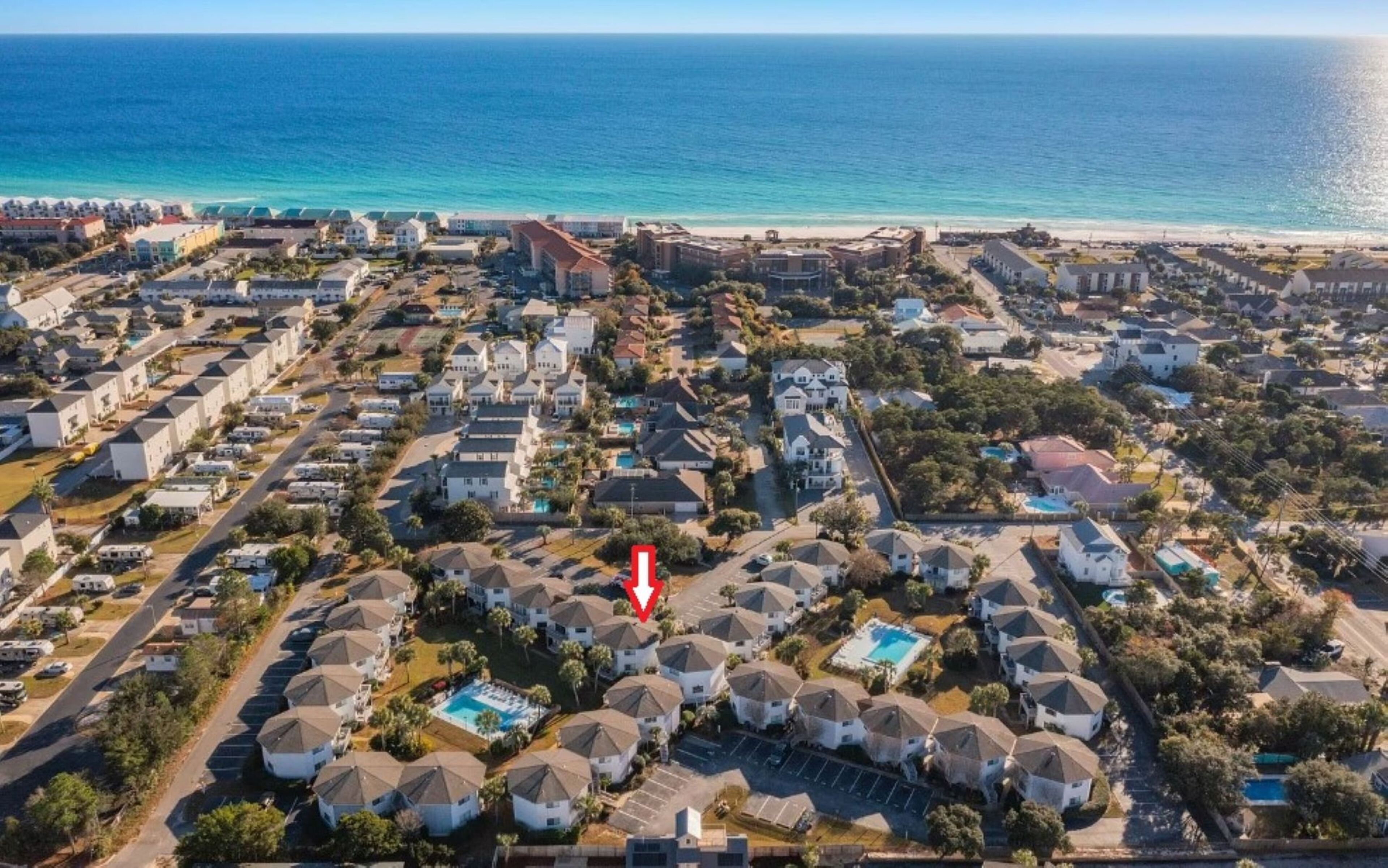 Vue aérienne d’un quartier résidentiel situé sur la côte, avec des maisons, une piscine et une plage en arrière-plan.