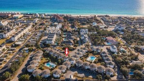 Vue aérienne d’un quartier résidentiel situé sur la côte, avec des maisons, une piscine et une plage en arrière-plan.